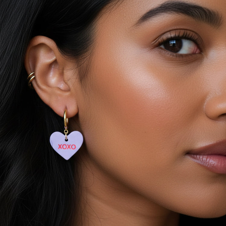 Close-up of a woman wearing gold hoop earrings with heart-shaped pendants.