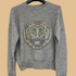Gray sweater with a tiger emblem on a hanger against a white background