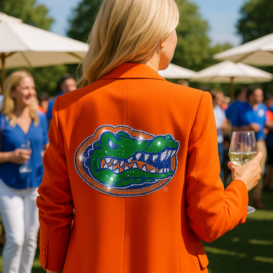 Person wearing an orange jacket with a gator logo, holding a glass of wine, in an outdoor setting.