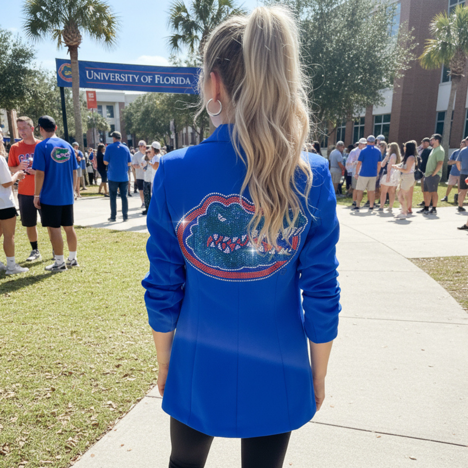 Person wearing a blue shirt with a logo on the back, standing on a sidewalk with people and palm trees in the background.