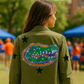 Person wearing a green jacket with a gator logo and stars, standing outdoors.