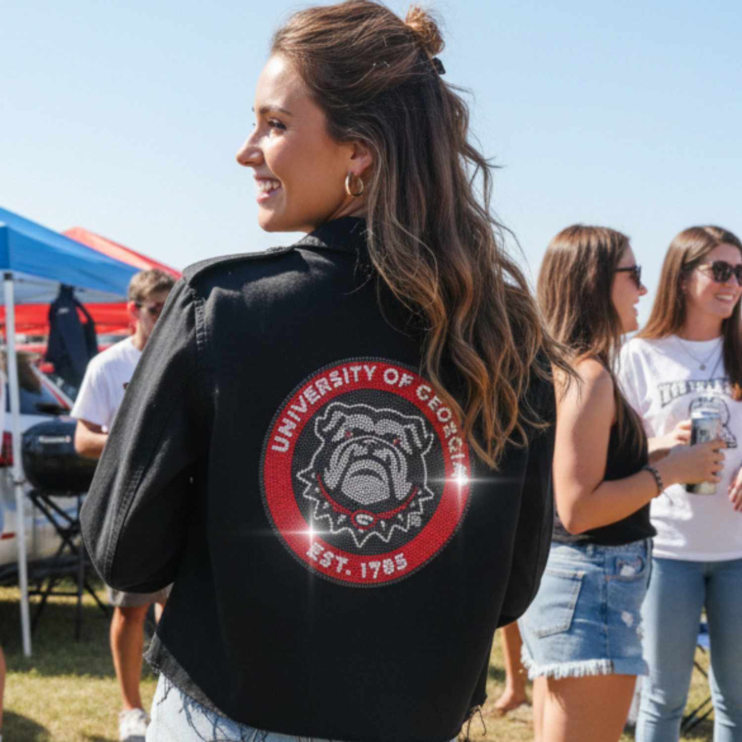 Woman wearing a black jacket with a university logo at an outdoor event.