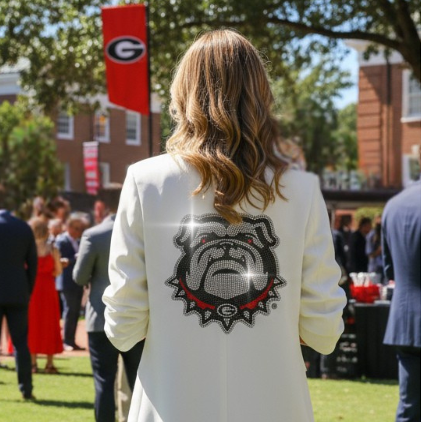 Person wearing a white blazer with a bulldog logo at an outdoor event.