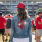 Person wearing a denim jacket with a helmet logo and red cap at a sports event.