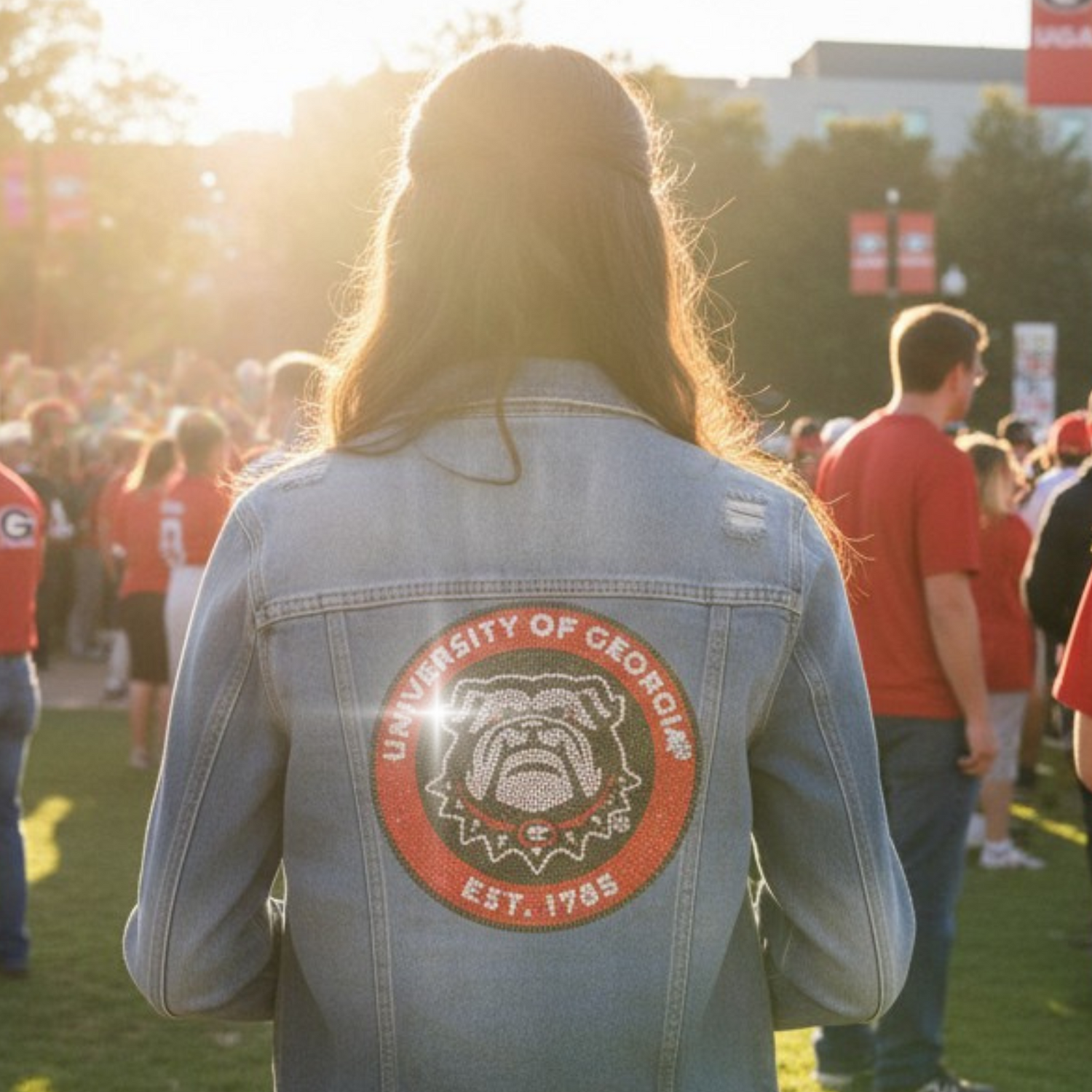 Person wearing a denim jacket with a University of Georgia logo at an outdoor event.