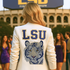 Person wearing a white jacket with LSU logo and tiger emblem in front of LSU stadium.