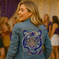 Woman wearing a denim jacket with a tiger design at a party.
