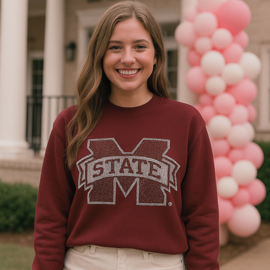 Woman wearing a Mississippi State sweatshirt in front of a building with pink and white balloons.