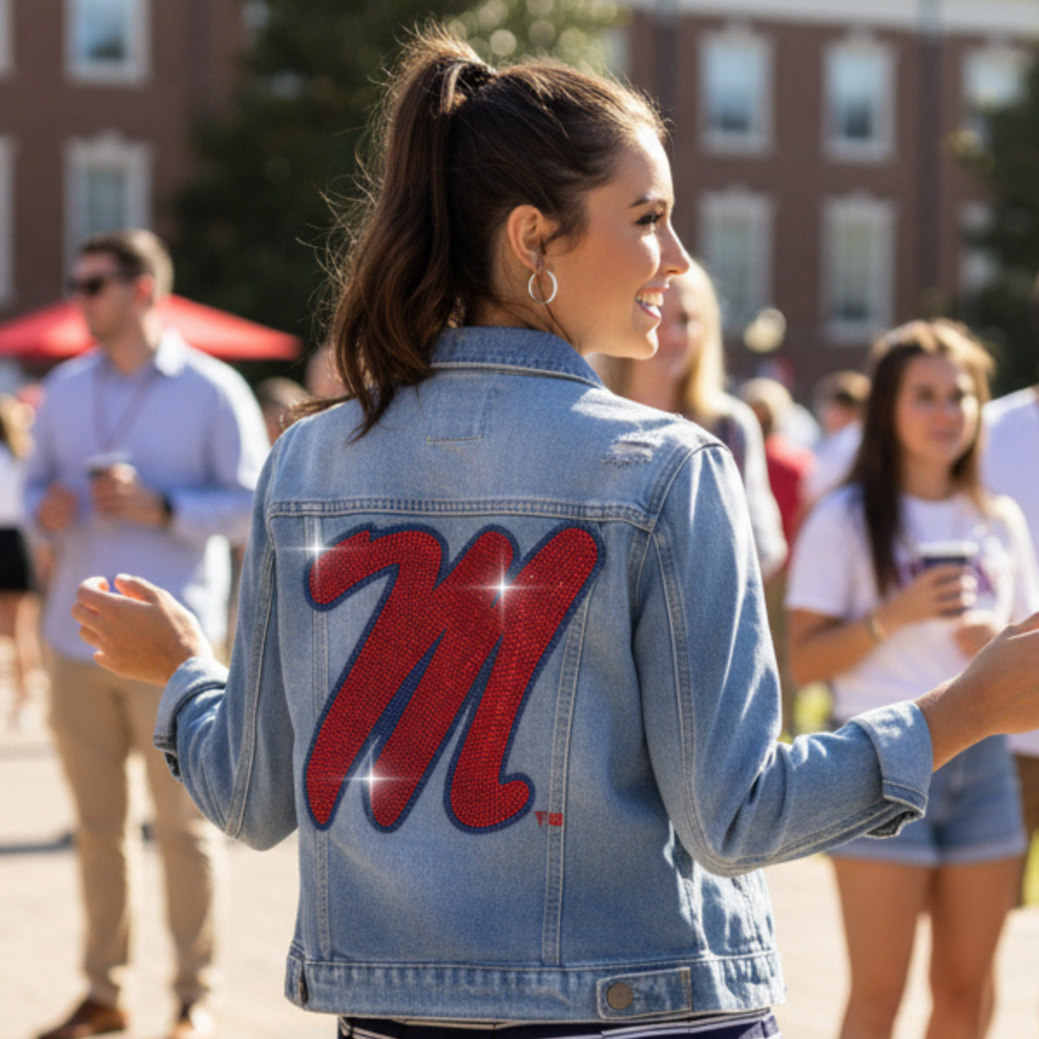 Woman wearing a denim jacket with a red 'M' on the back, standing outdoors.