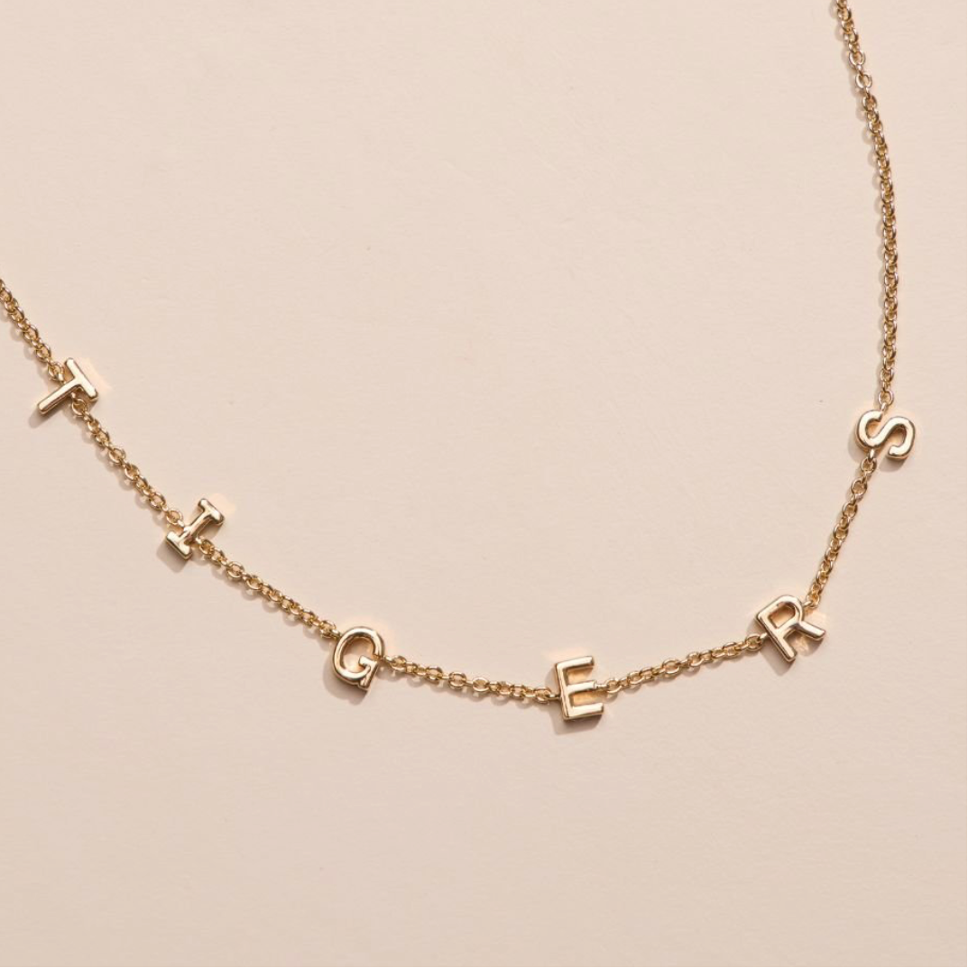 Gold necklace with small letter pendants on a beige background
