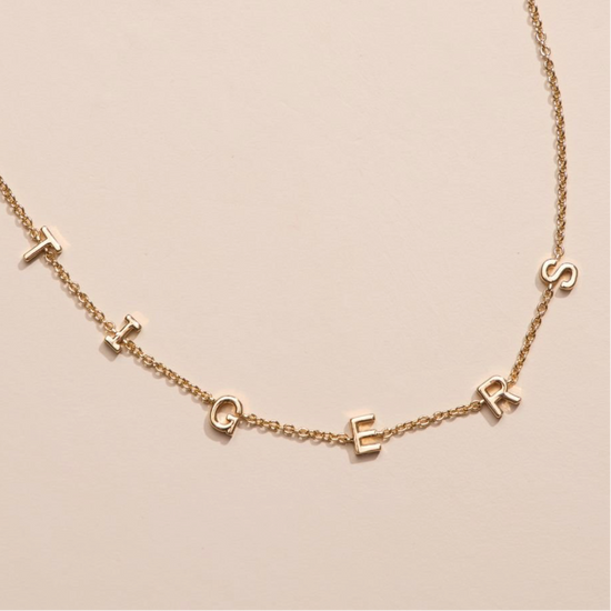 Gold necklace with small letter pendants on a beige background