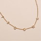 Gold necklace with small letter pendants on a beige background