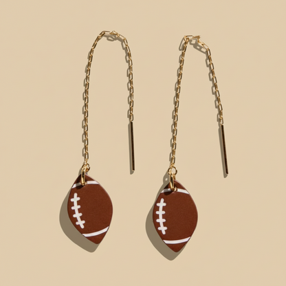 Football-shaped earrings with gold chains on a white background