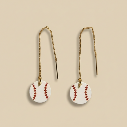 Baseball-shaped earrings on thin strings against a white background