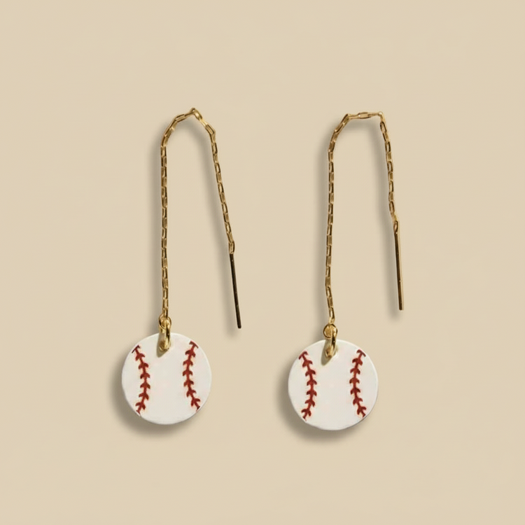 Baseball-shaped earrings on thin strings against a white background