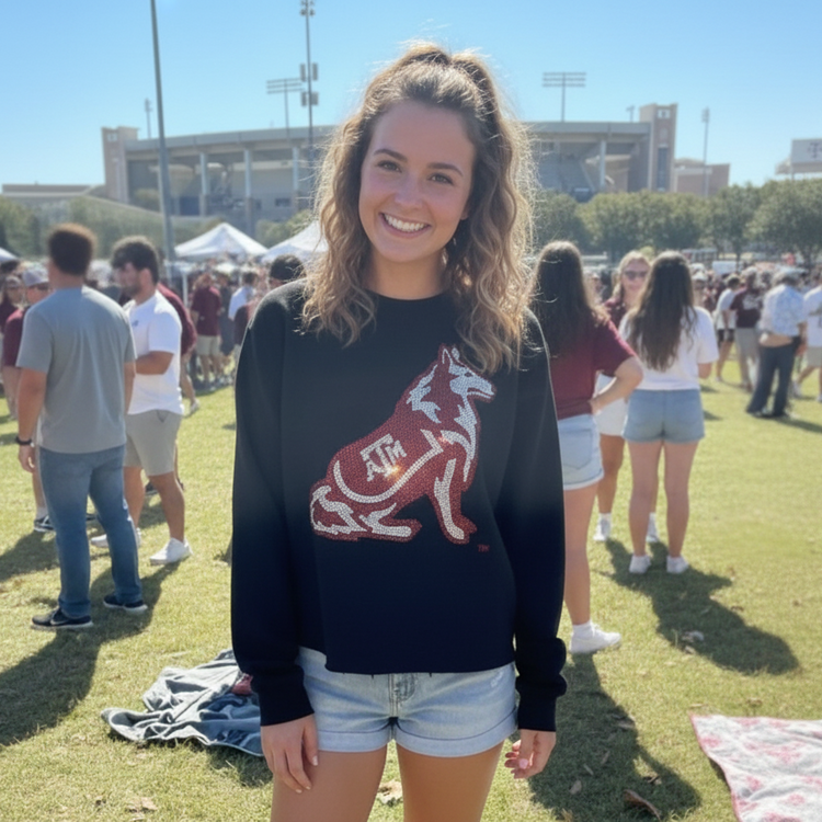 Woman wearing a navy sweatshirt with a red and white logo on a grassy field with people in the background.