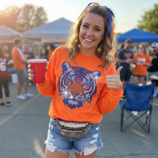 Woman in orange sweatshirt with tiger logo, denim shorts, and fanny pack at outdoor event.