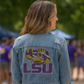 Person wearing a denim jacket with LSU logo in an outdoor setting