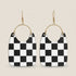 Black and white checkered earrings with gold hoop accents on a beige background