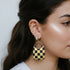 Checkered earring worn by a person with dark hair.