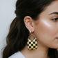 Checkered earring worn by a person with dark hair.