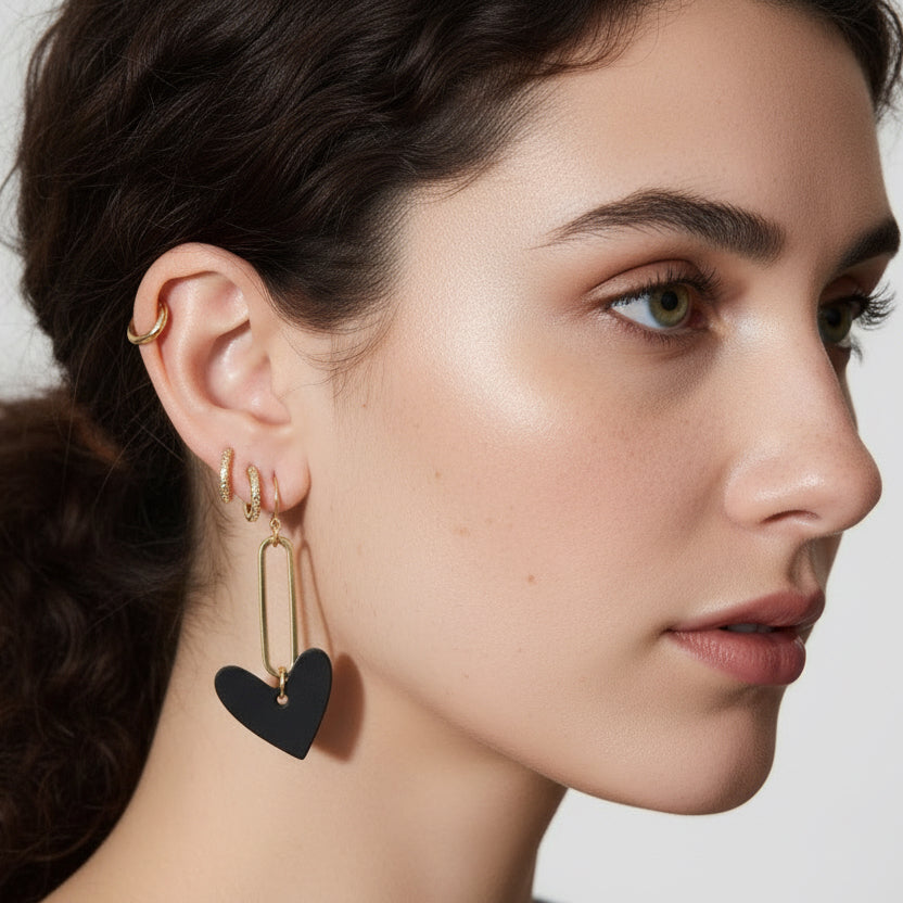 Close-up of a person wearing a black heart-shaped earring with a gold hoop.