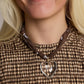 Close-up of a person wearing a necklace with a heart pendant, dressed in a brown checkered outfit.