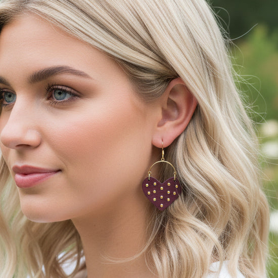 Close-up of a person wearing heart-shaped earrings with a blurred outdoor background
