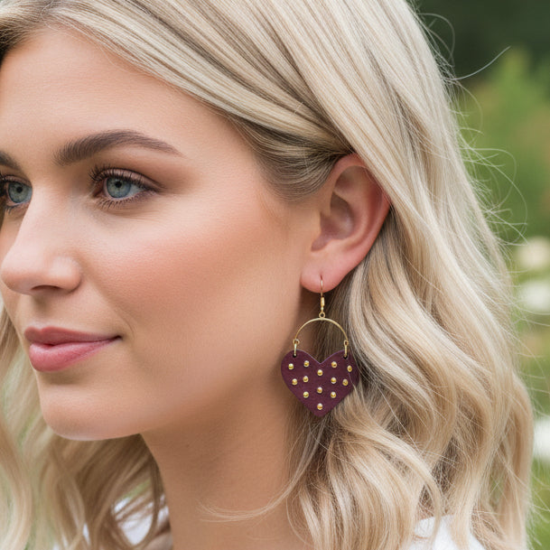 Close-up of a person wearing heart-shaped earrings with a blurred outdoor background