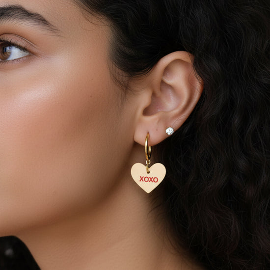 Close-up of a woman wearing gold heart-shaped earrings with &