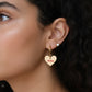 Close-up of a woman wearing gold heart-shaped earrings with &