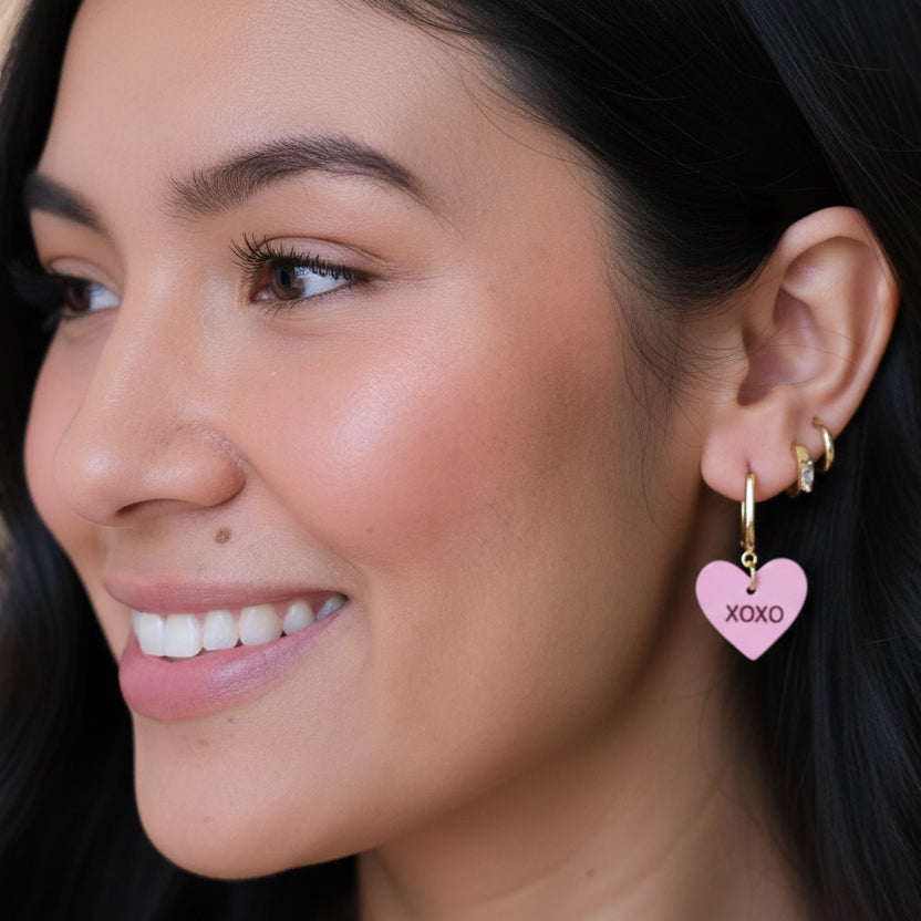 Close-up of a woman wearing a pink heart-shaped earring with &