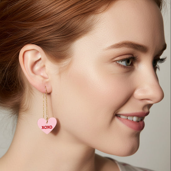 Close-up of a person wearing pink heart-shaped earrings with &