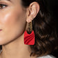 Close-up of a person wearing a red earring with a gold chain.
