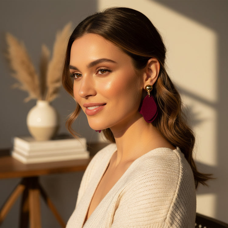 Pair of burgundy earrings with gold posts on a beige background