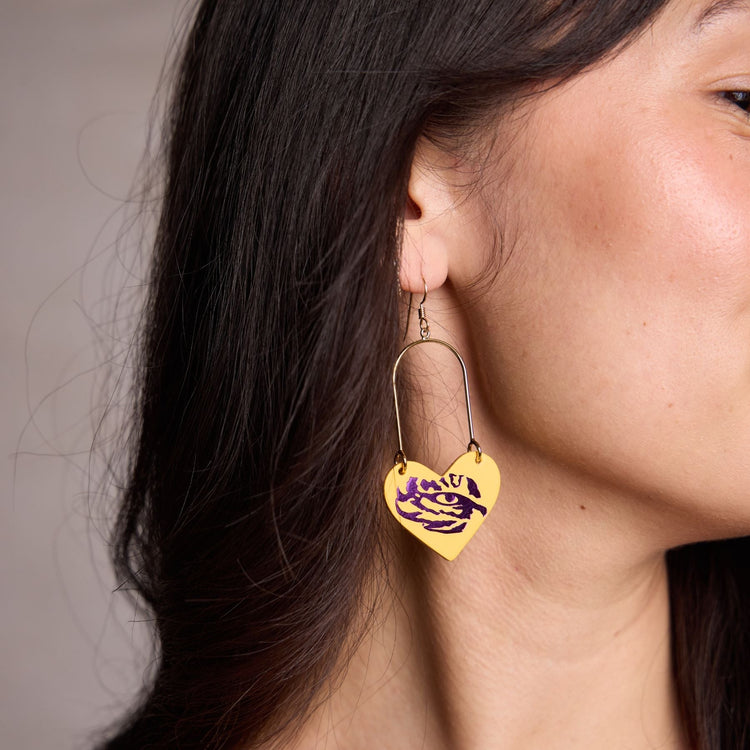 Heart-shaped earrings with purple design worn by a person against a neutral background