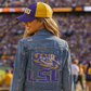 Person wearing a LSU denim jacket and cap on a sports field