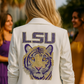 Person wearing a white blazer with LSU tiger logo, standing outdoors with blurred people in the background.