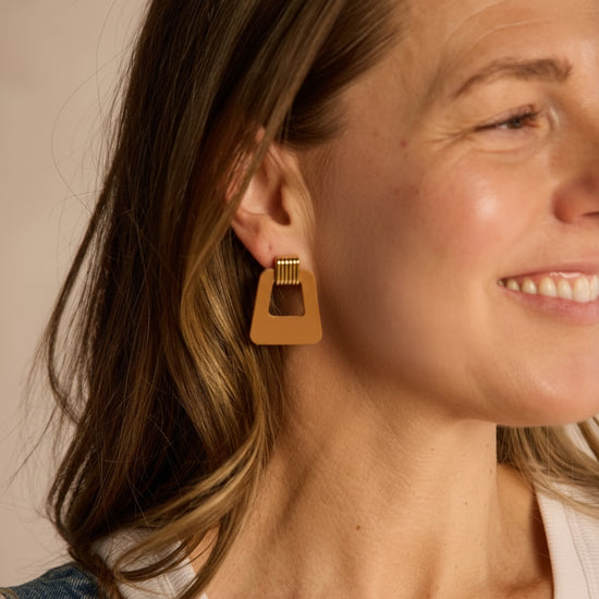 Close-up of a woman wearing gold earrings with a neutral background