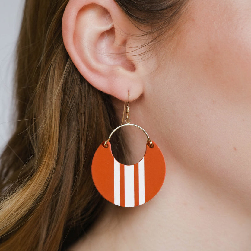 Close-up of a person wearing a round earring with a brown center and red stripes.