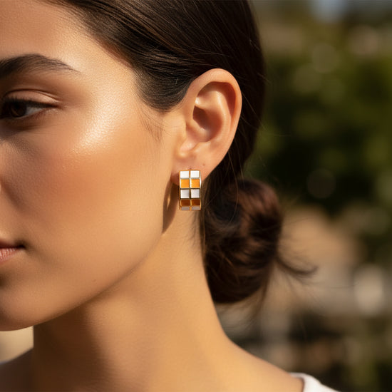 Pair of gold hoop earrings with orange and white checkered pattern on a beige background