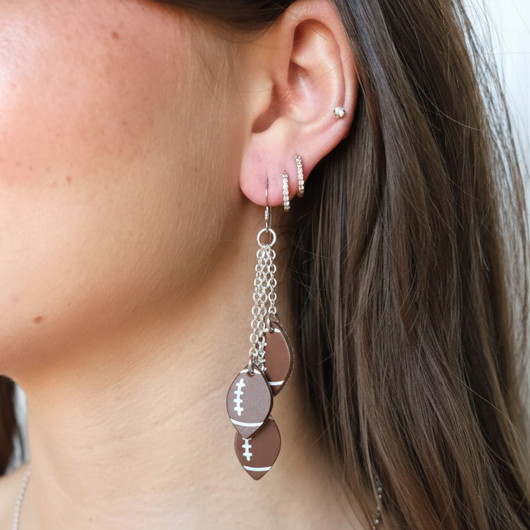 Close-up of an ear wearing a silver earring with football-shaped charms.