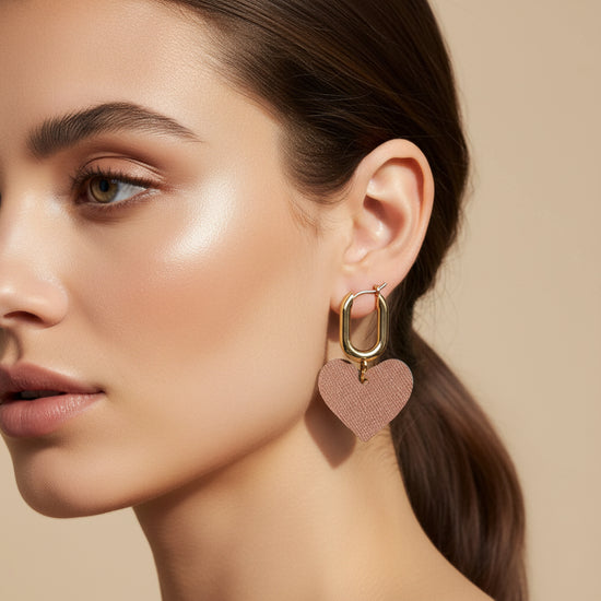 Gold hoop earrings with pink heart charms on a beige background