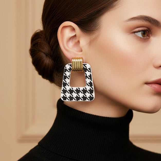 Pair of black and white houndstooth patterned earrings with gold accents on a beige background